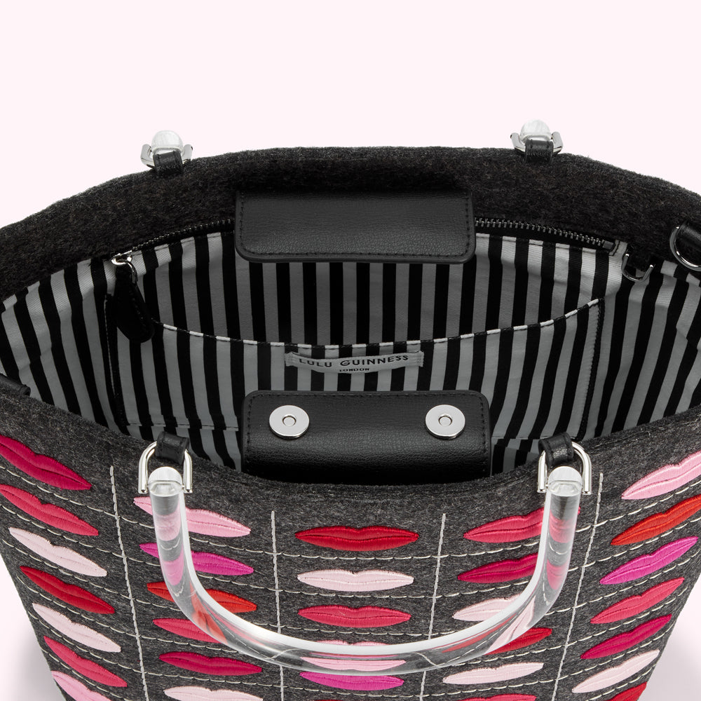 Grey felt tote bag with embroidered lips and clear acrylic handles, showing the black and white striped interior.