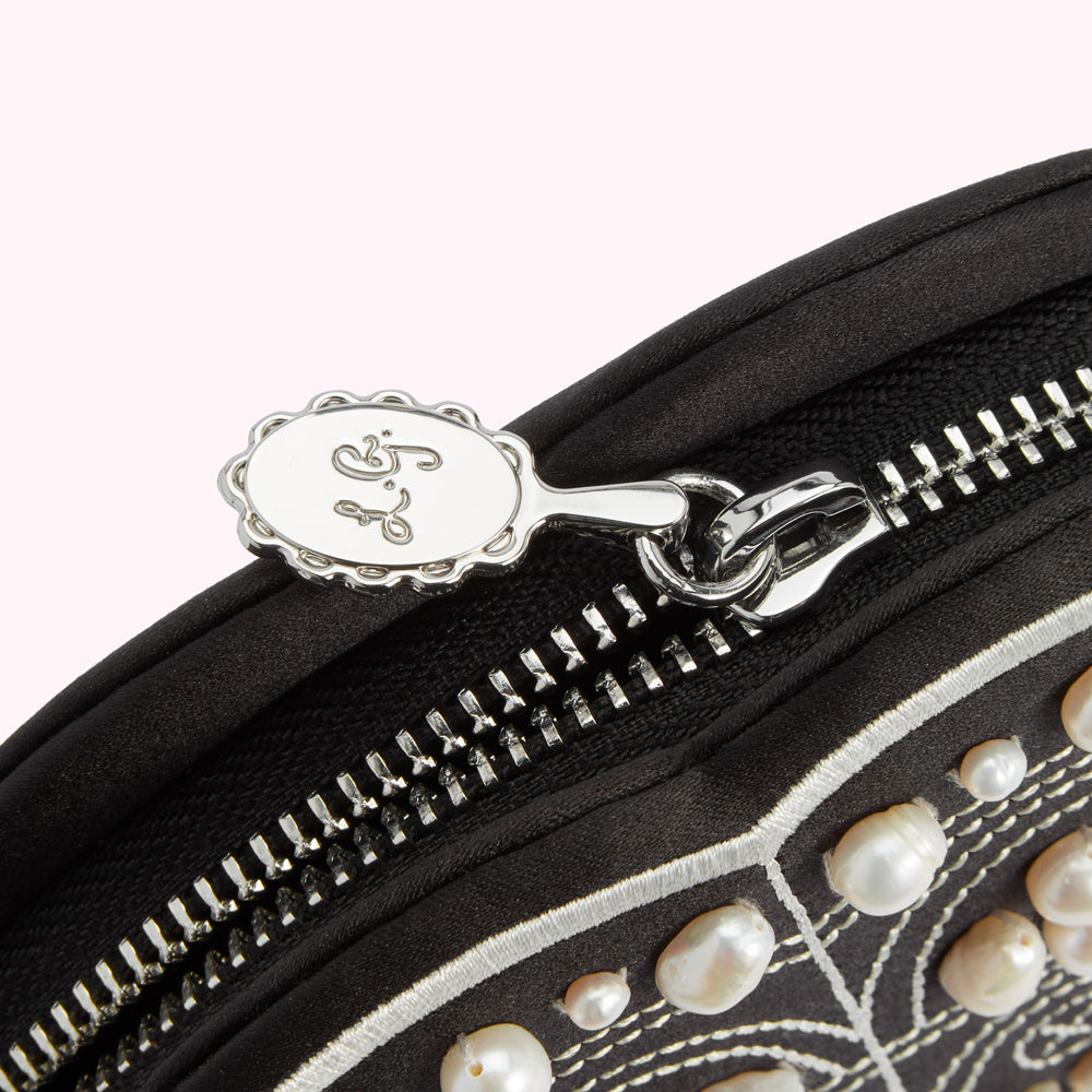 Close-up of a black, pearl-embellished purse's zipper and charm, which is oval-shaped and engraved with the brand's logo.