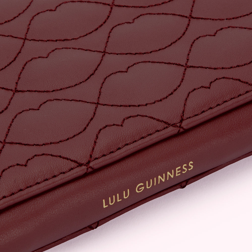 Close-up of a burgundy Lulu Guinness wallet with a lip-shaped quilted pattern and the brand name embossed in gold.
