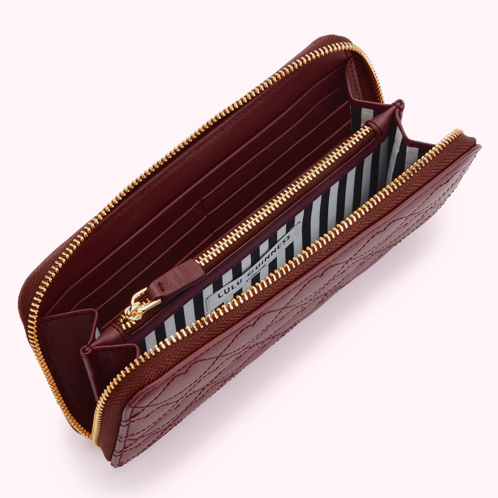 Open burgundy quilted zip-around wallet with gold zippers and black and white striped interior lining.
