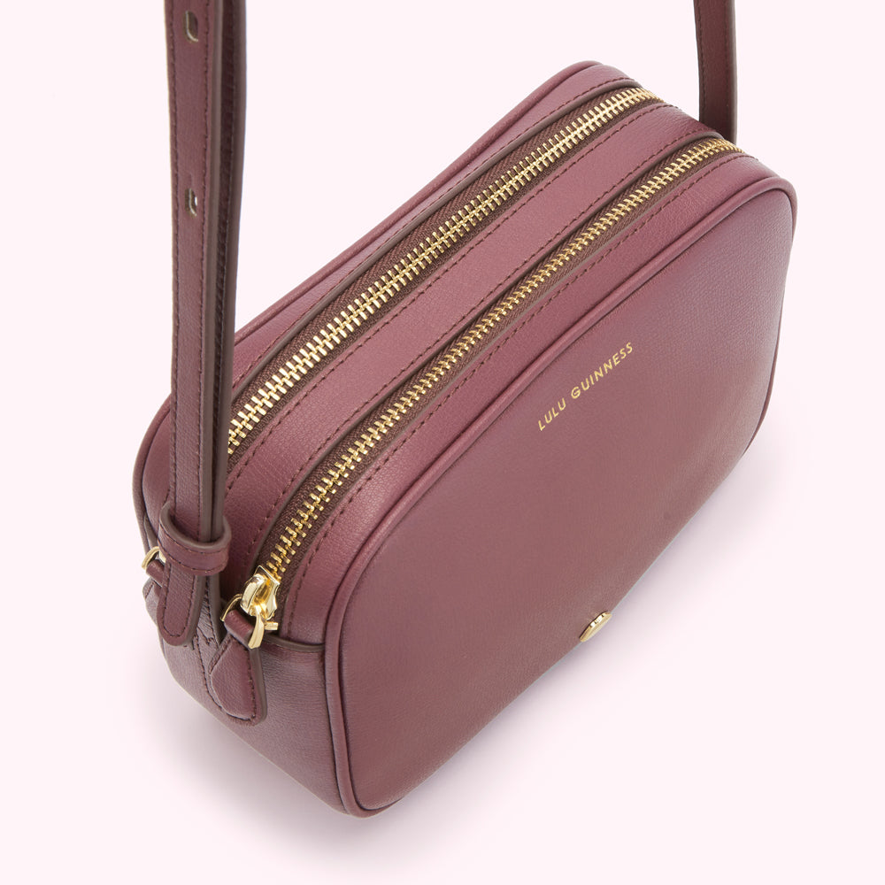A burgundy Lulu Guinness crossbody bag with two gold zippers.