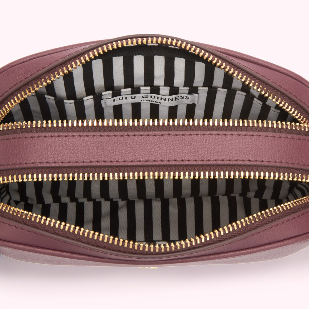Inside of a mauve Lulu Guinness crossbody bag with gold zippers and black and white striped lining.