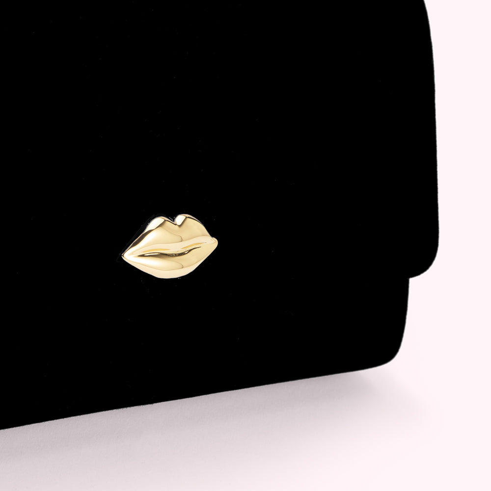 Close-up of a black velvet clutch with a gold lip-shaped detail.
