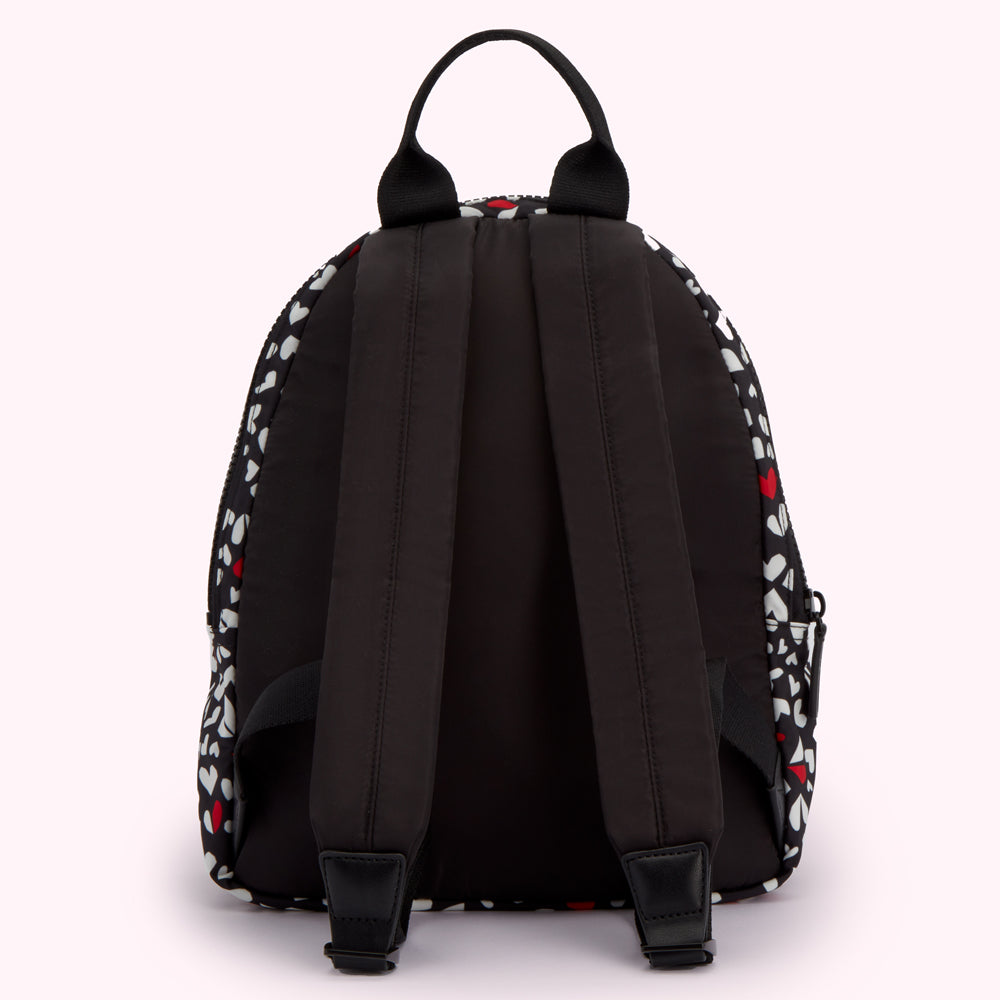 Black backpack with white and red heart pattern, viewed from the back.

