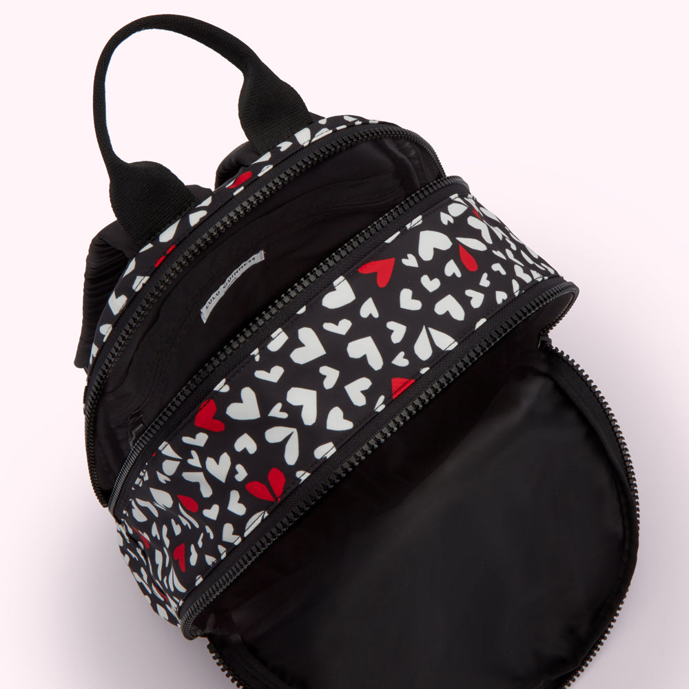 Black backpack with white and red hearts pattern, open to show the inside.
