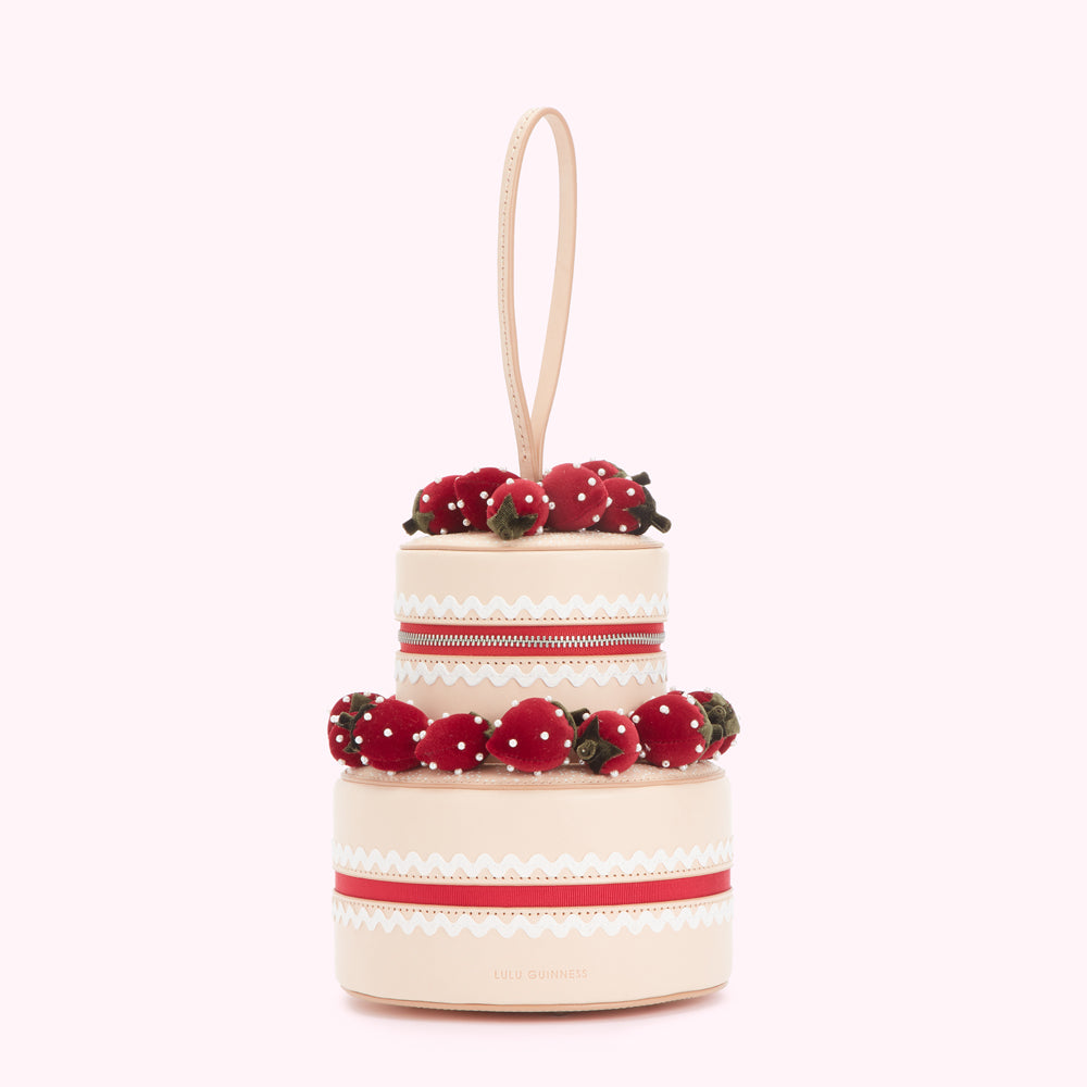 Two-tiered strawberry cake-shaped handbag in beige with red and white details.
