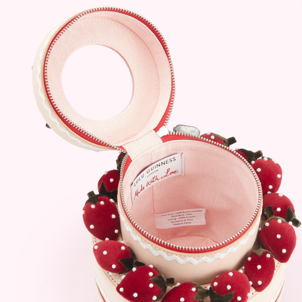 Open strawberry cake-shaped handbag with pink interior and label reading "Lulu Guinness London Made with Love".