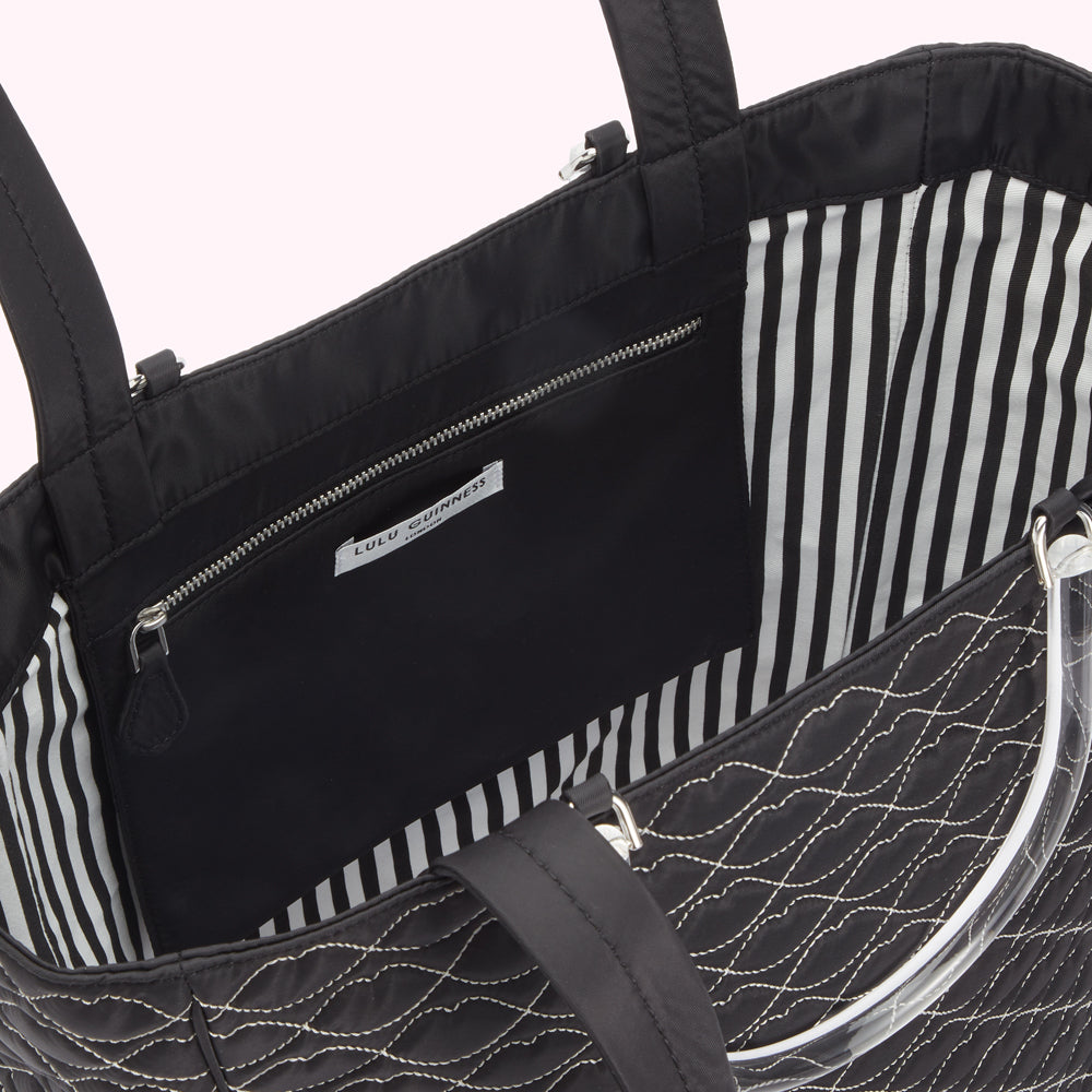 Interior view of a black quilted Lulu Guinness tote bag with a black and white striped lining and a clear acrylic handle.
