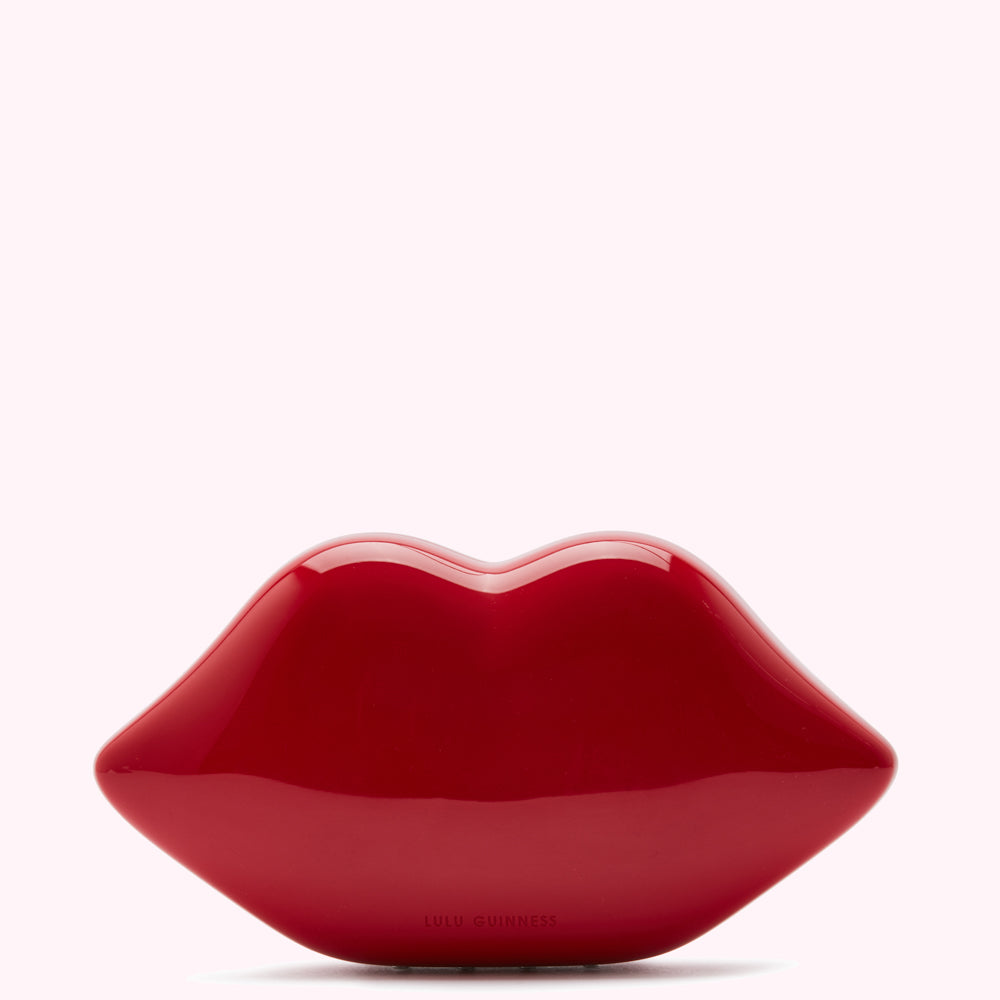 Red Lulu Guinness lip-shaped clutch against a white background.

