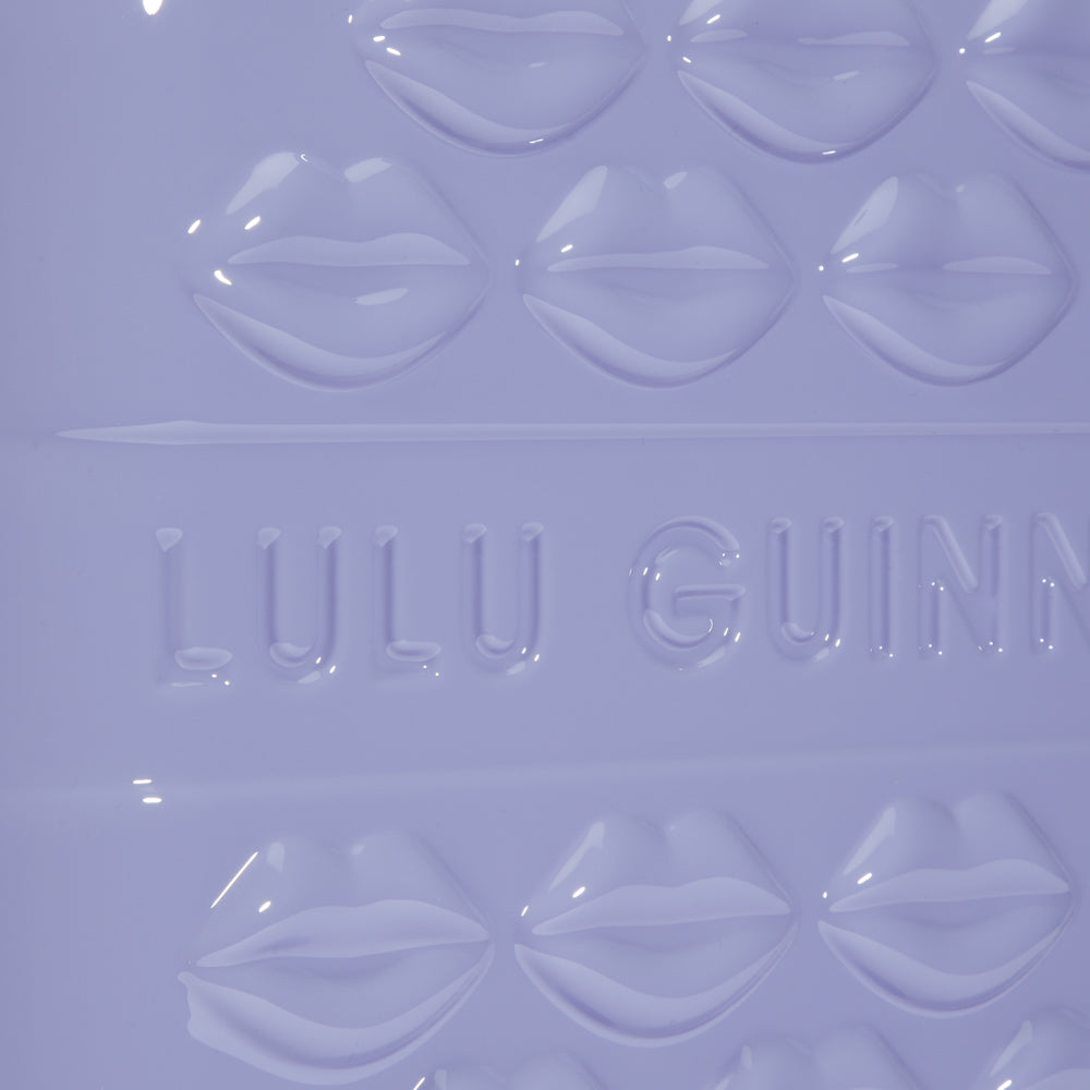 Close-up of a lavender-coloured Lulu Guinness item featuring embossed lips and the brand's logo.
