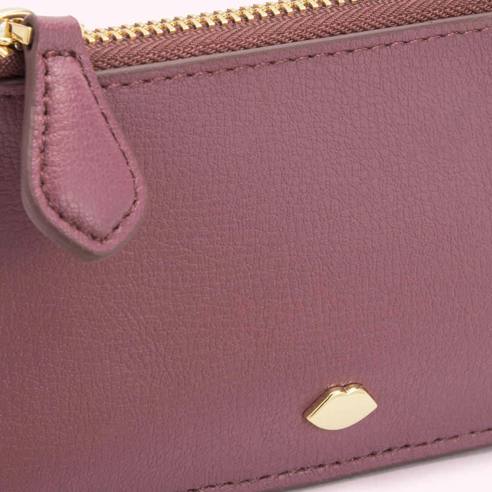 Close-up of a mauve leather zip-around wallet with a gold zipper and a small gold lip-shaped logo.
