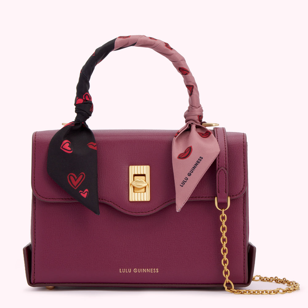 Burgundy Lulu Guinness satchel bag with gold hardware and a detachable shoulder strap. The bag features a black and mauve patterned scarf handle.
