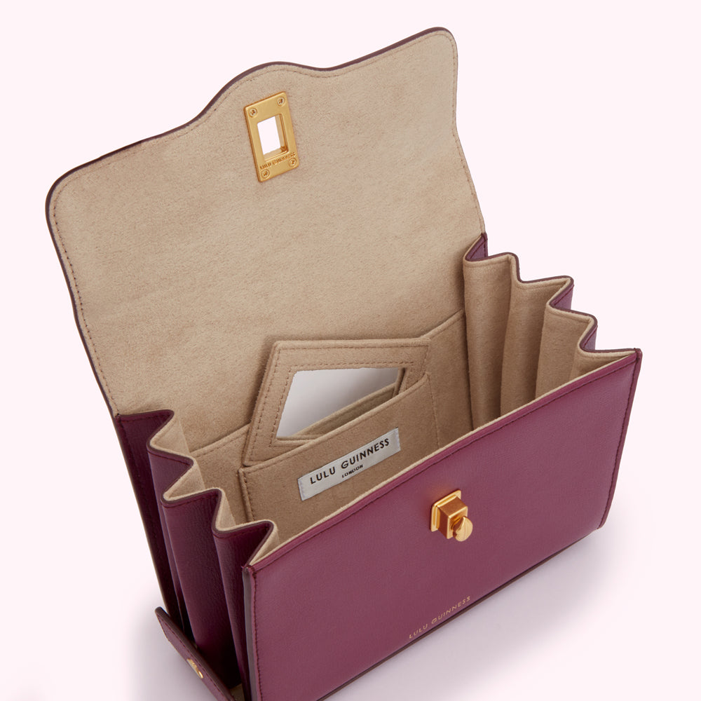 Open burgundy Lulu Guinness handbag with beige interior and gold accents.
