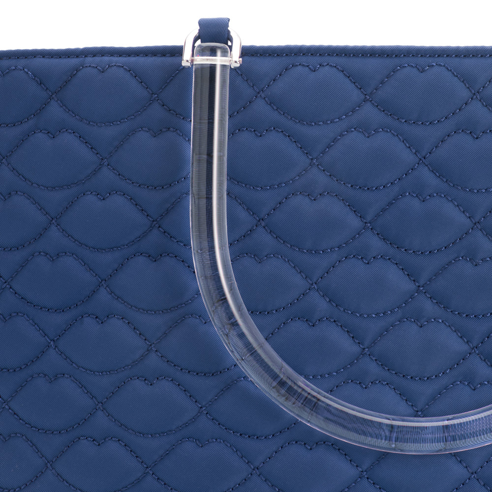 Close-up of a navy blue quilted handbag with a clear acrylic handle; the quilting is patterned with lip shapes.
