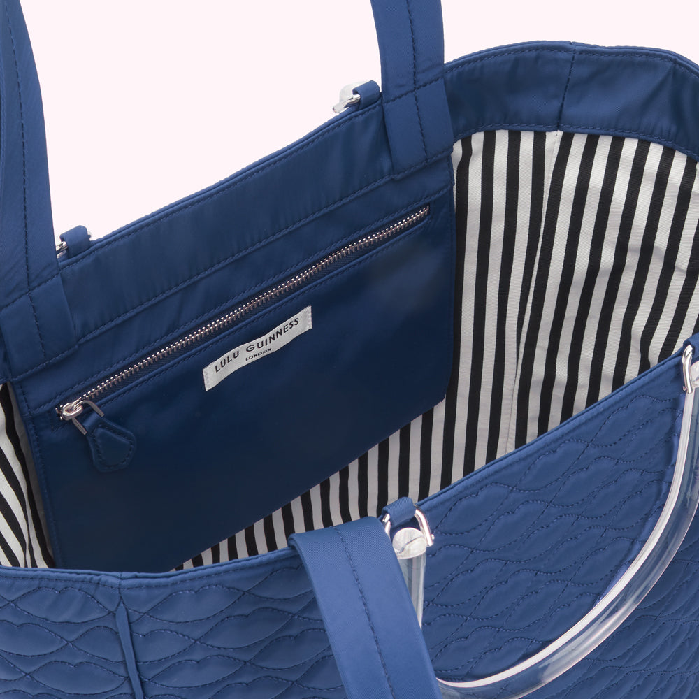 Inside view of a navy blue Lulu Guinness tote bag with a black and white striped lining and a clear handle.