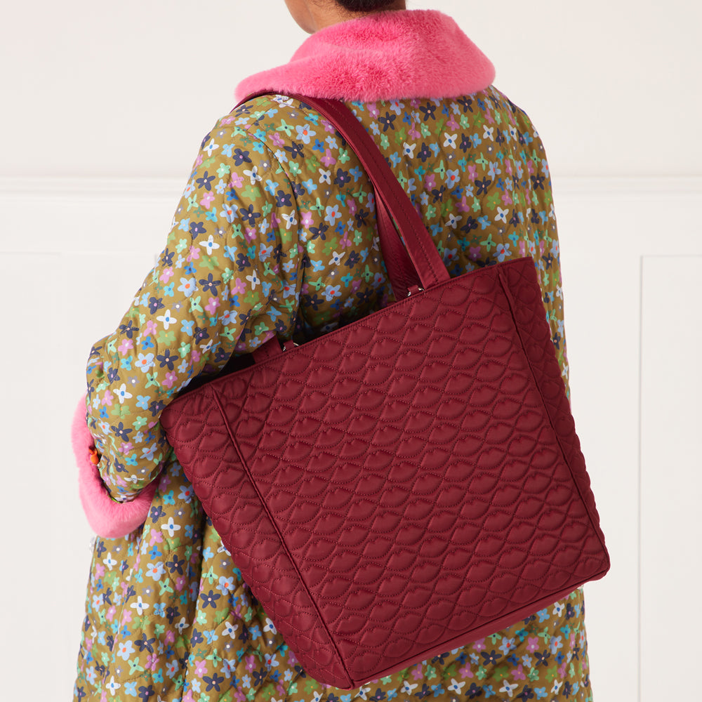 Burgundy quilted tote bag with a lip print pattern on a floral quilted coat.
