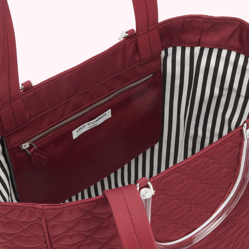 Burgundy quilted tote bag with black and white striped interior and clear handles. The interior features a burgundy zippered pocket with a Lulu Guinness London label.

