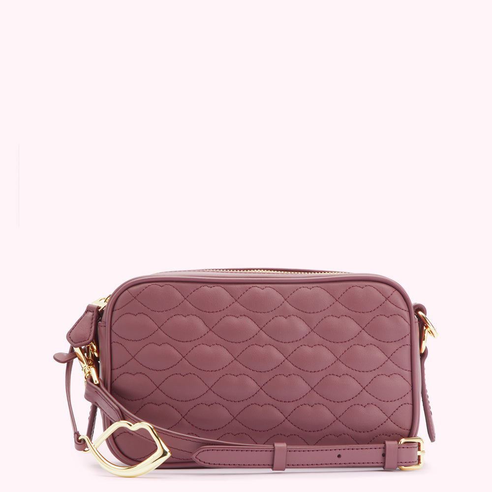 A dusty rose quilted crossbody bag with gold lip-shaped detail on the strap.
