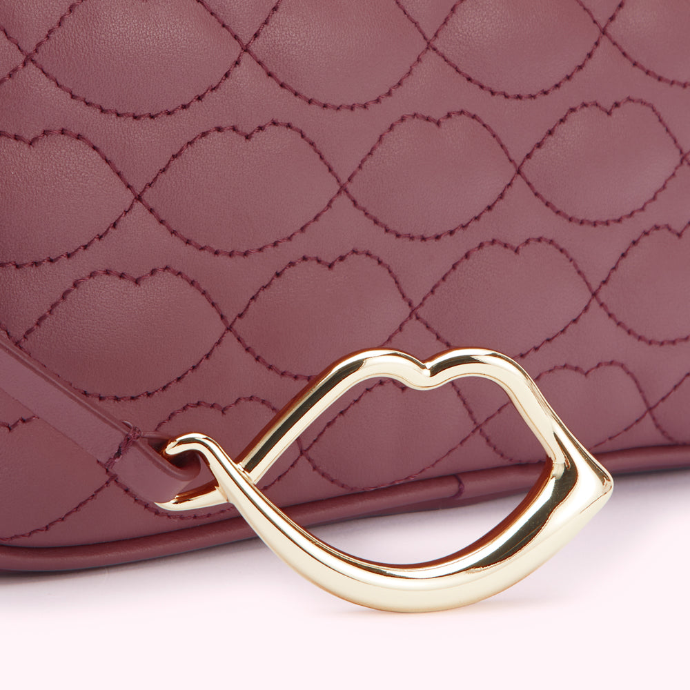 Close-up of a burgundy quilted handbag with a gold lip-shaped accent.