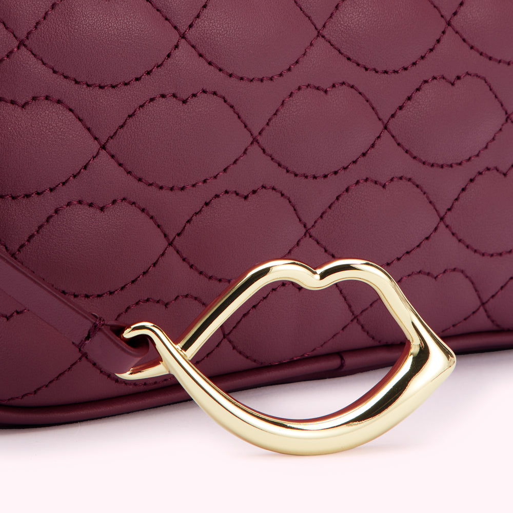 Close-up of a burgundy quilted handbag with a gold lip-shaped handle.
