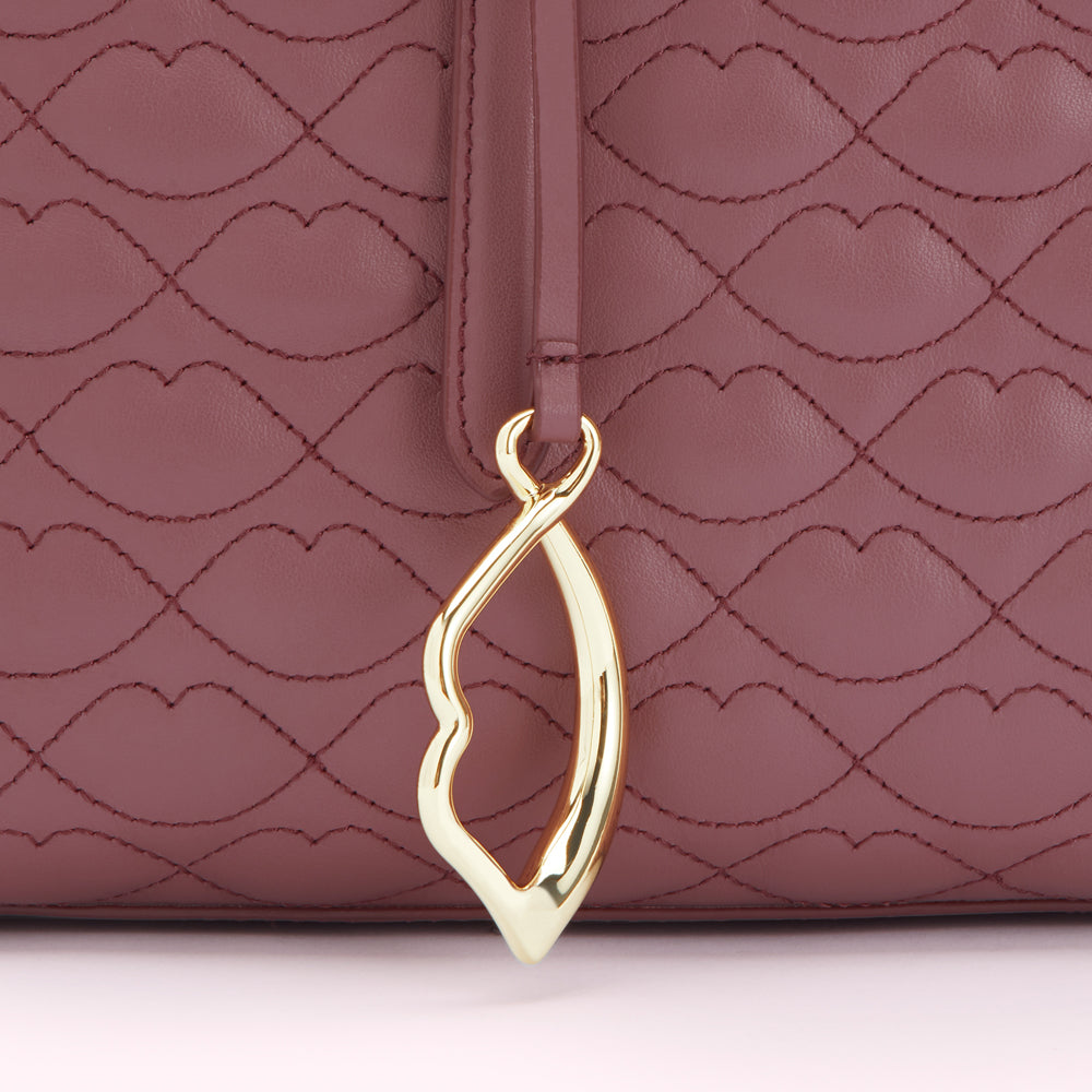 Close-up of a mauve quilted handbag with a gold lip-shaped charm.