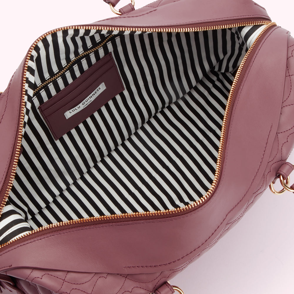 Inside view of a mauve quilted Lulu Guinness handbag with black and white striped lining.