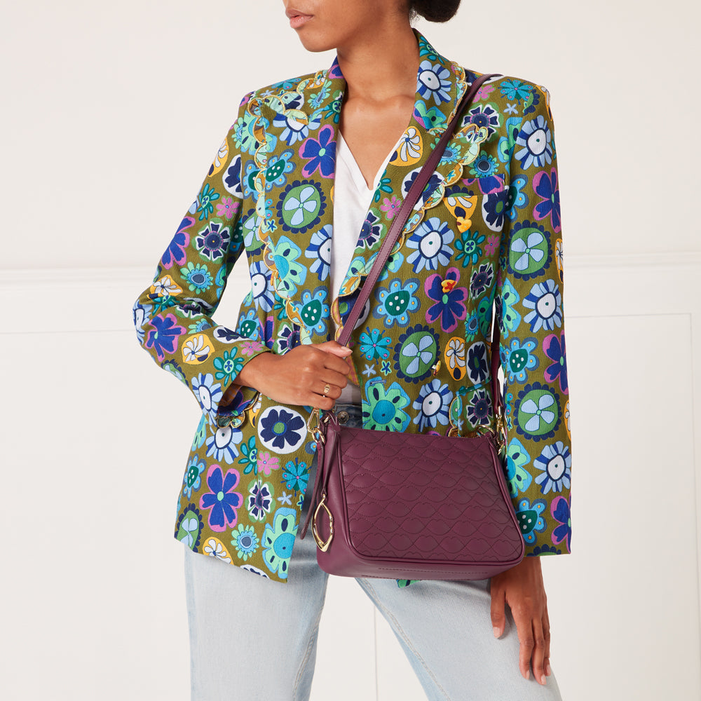 A woman in a floral blazer carries a quilted purple crossbody bag.