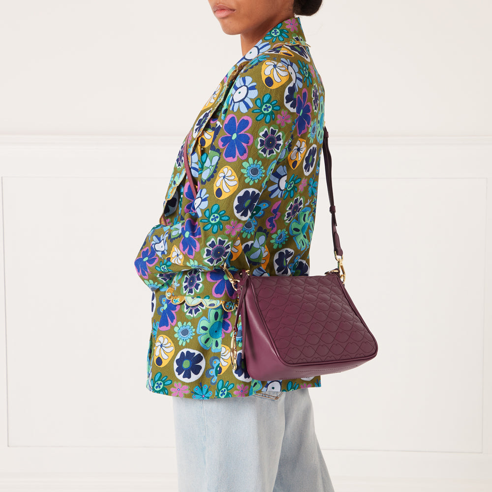A woman in a floral blazer carries a quilted purple crossbody bag.
