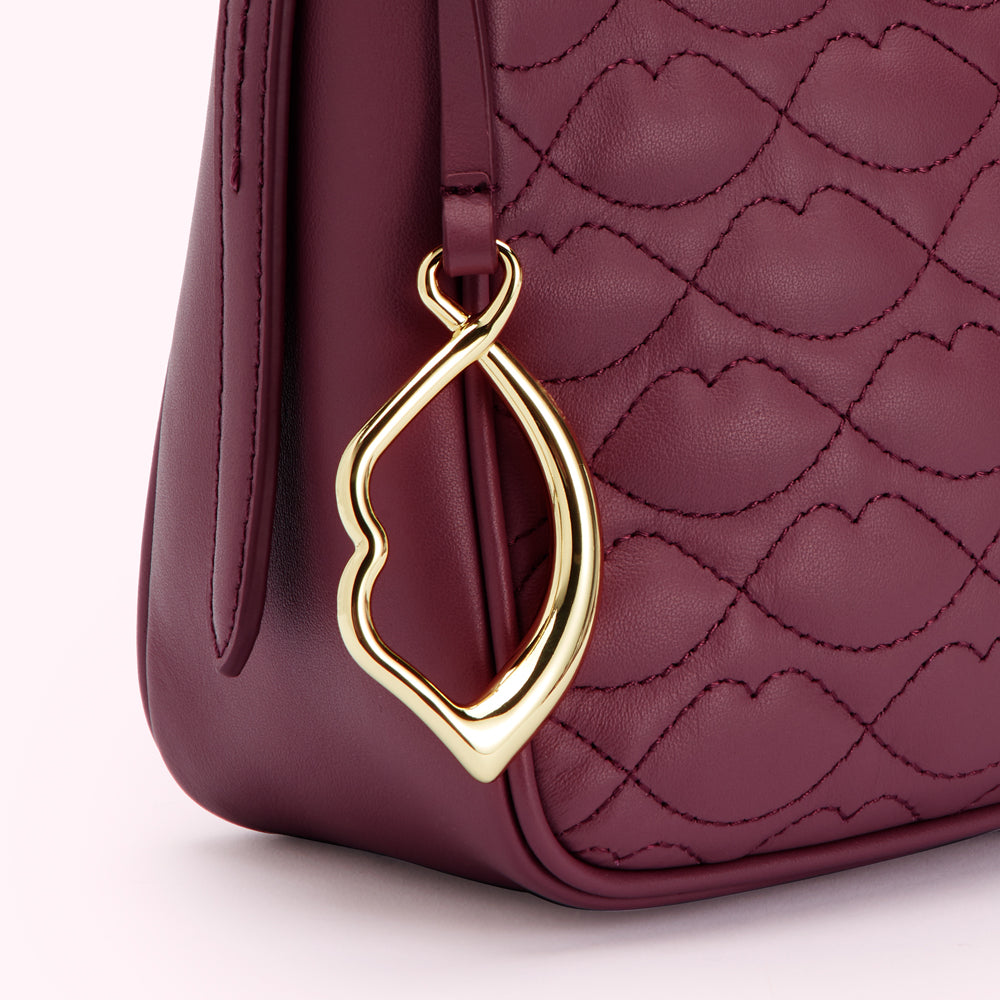 Close-up of a burgundy quilted handbag with a gold lip-shaped charm.
