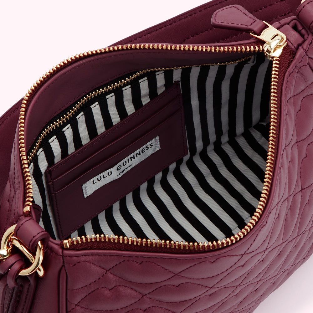 Inside of a burgundy quilted Lulu Guinness London handbag, showing the black and white striped lining and a burgundy internal pocket.
