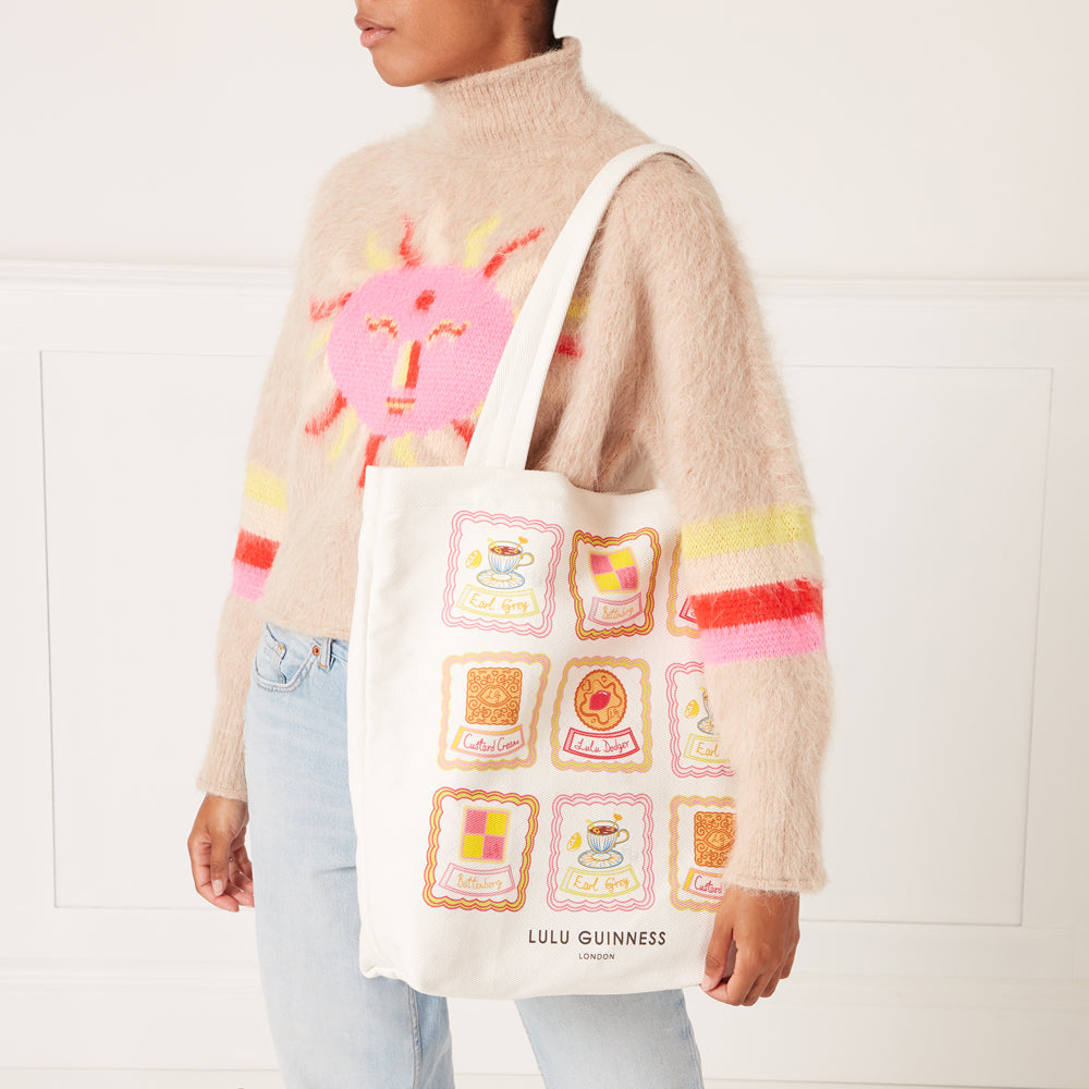 Person holding a Lulu Guinness tote bag with a biscuit design against a white background.