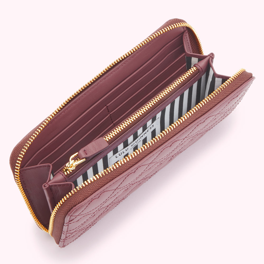 Open burgundy quilted zip-around wallet by Lulu Guinness, featuring a black and white striped interior.

