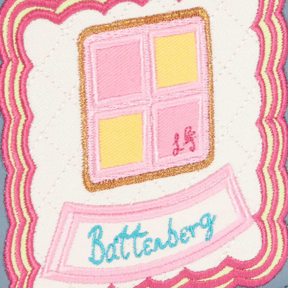 Embroidered patch depicting a Battenberg cake on a cream background with a pink and yellow design, surrounded by a scalloped pink and yellow border. The word "Battenberg" is embroidered in teal.
