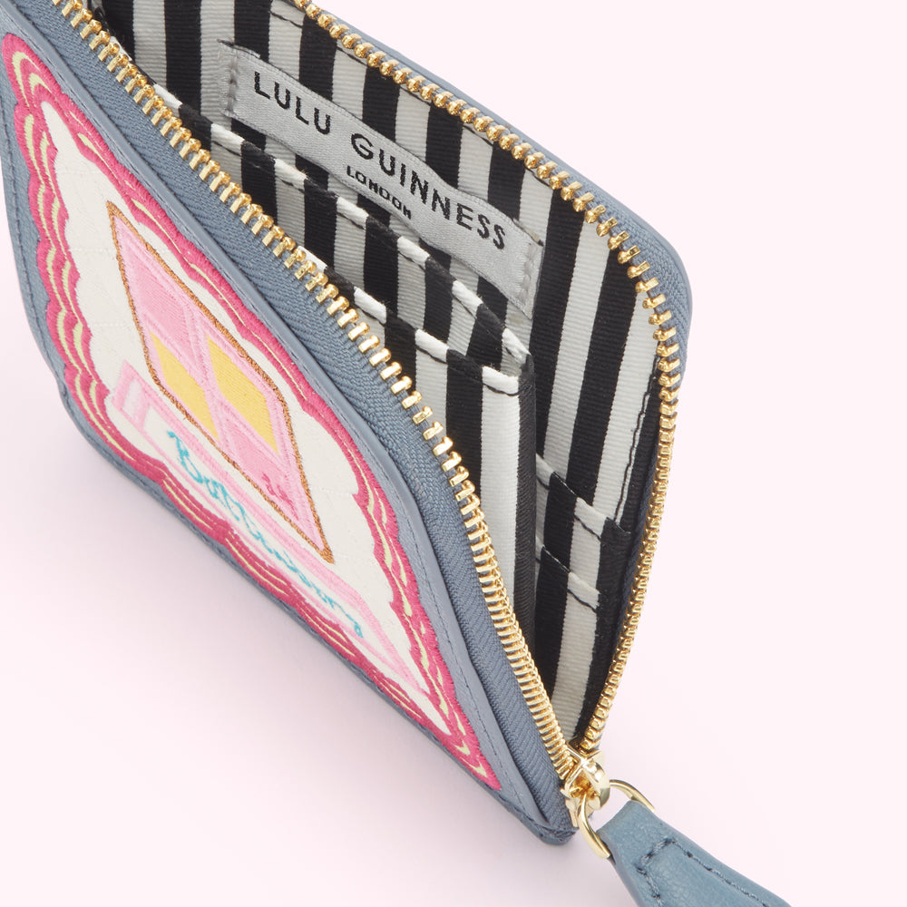 A grey Lulu Guinness zip-around purse with an embroidered pink and yellow house design on the front, partially open to show the black and white striped interior lining.
