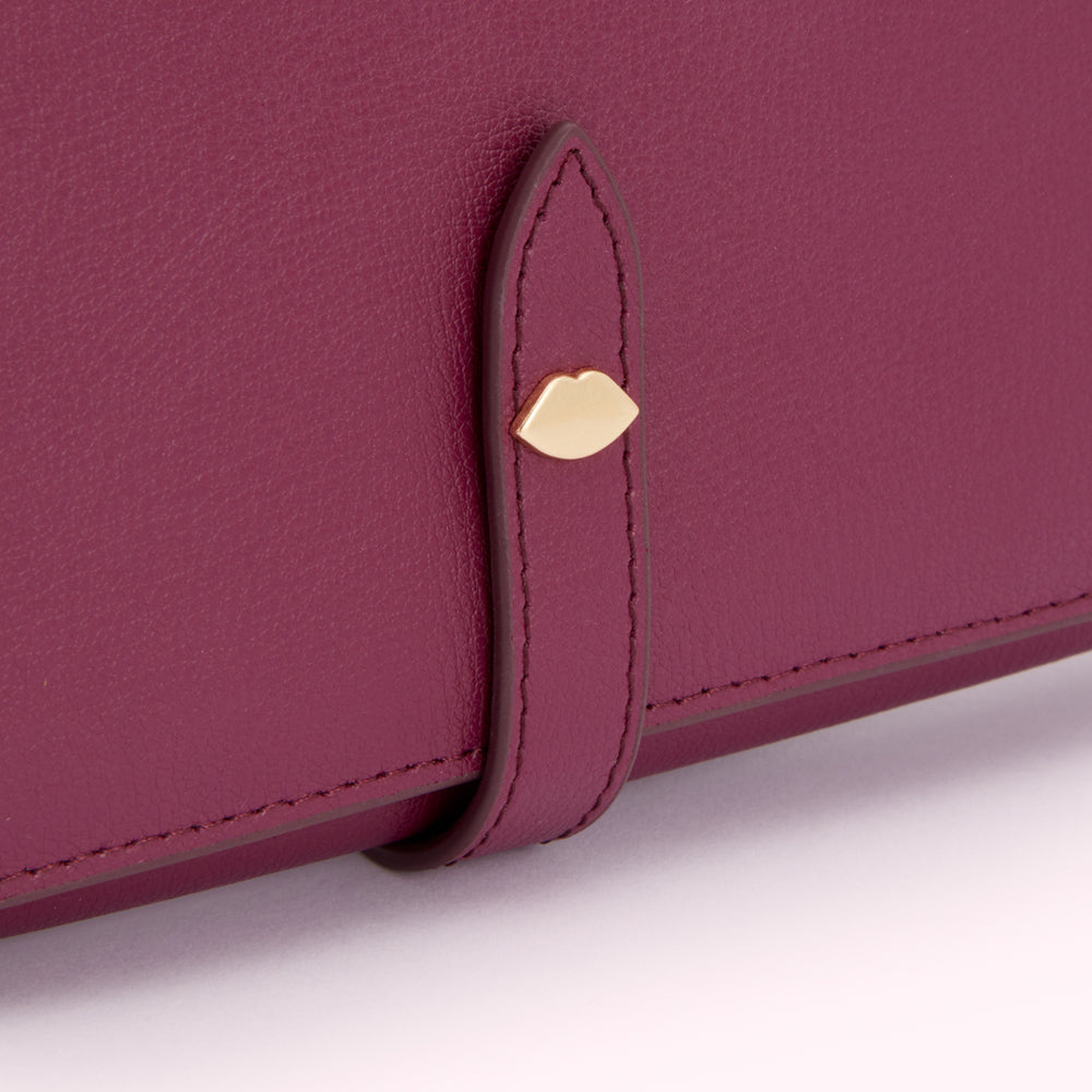 Close-up of a burgundy leather wallet with a gold lip-shaped detail on the strap.
