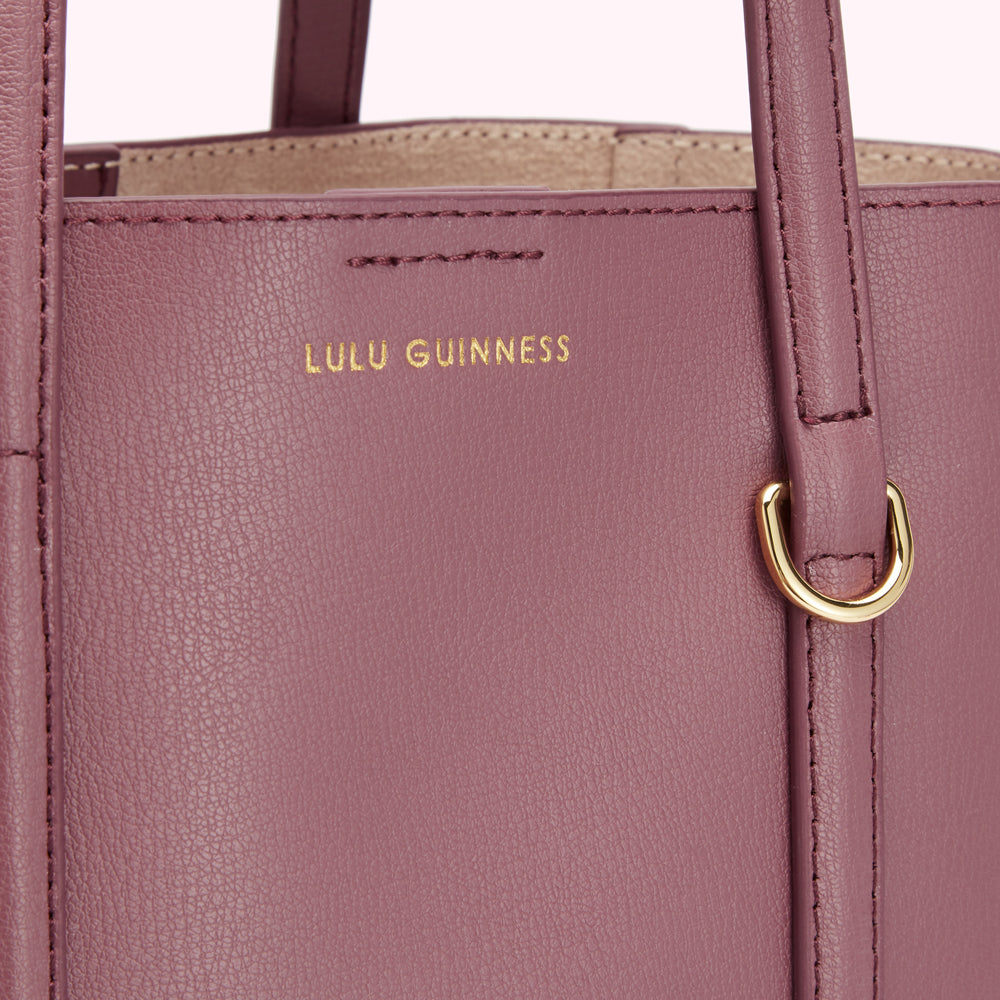 Close-up of a dusty rose Lulu Guinness tote bag showing the brand's name embossed on the front.
