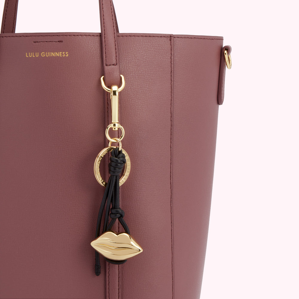 Close-up of a dusty rose Lulu Guinness tote bag with a gold lip-shaped keychain.