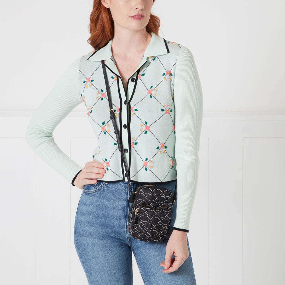 Woman wearing a mint green cardigan with floral embroidery and black crossbody bag.
