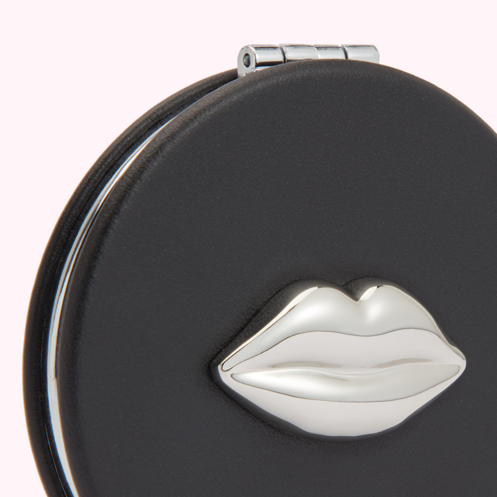 Close-up of a black compact mirror with a silver lip design.
