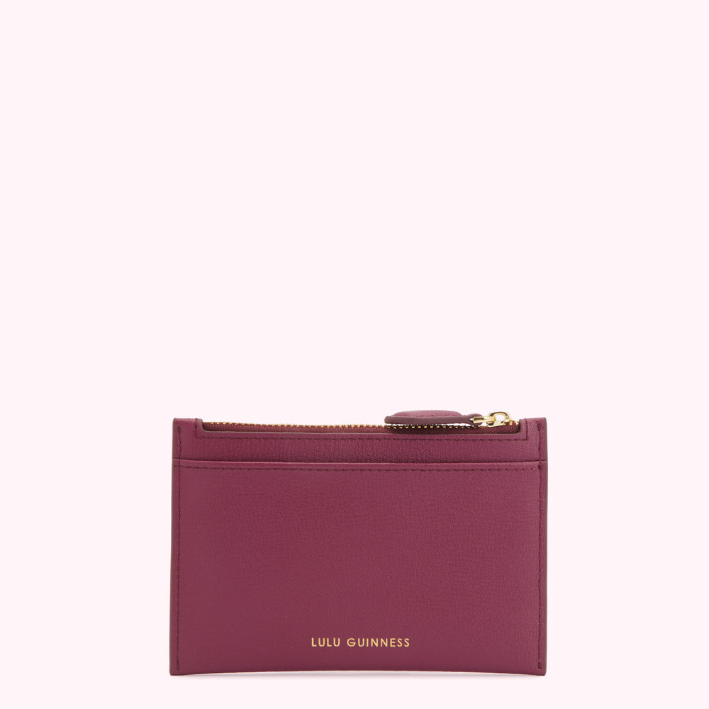 A burgundy Lulu Guinness zip-around cardholder against a white background.
