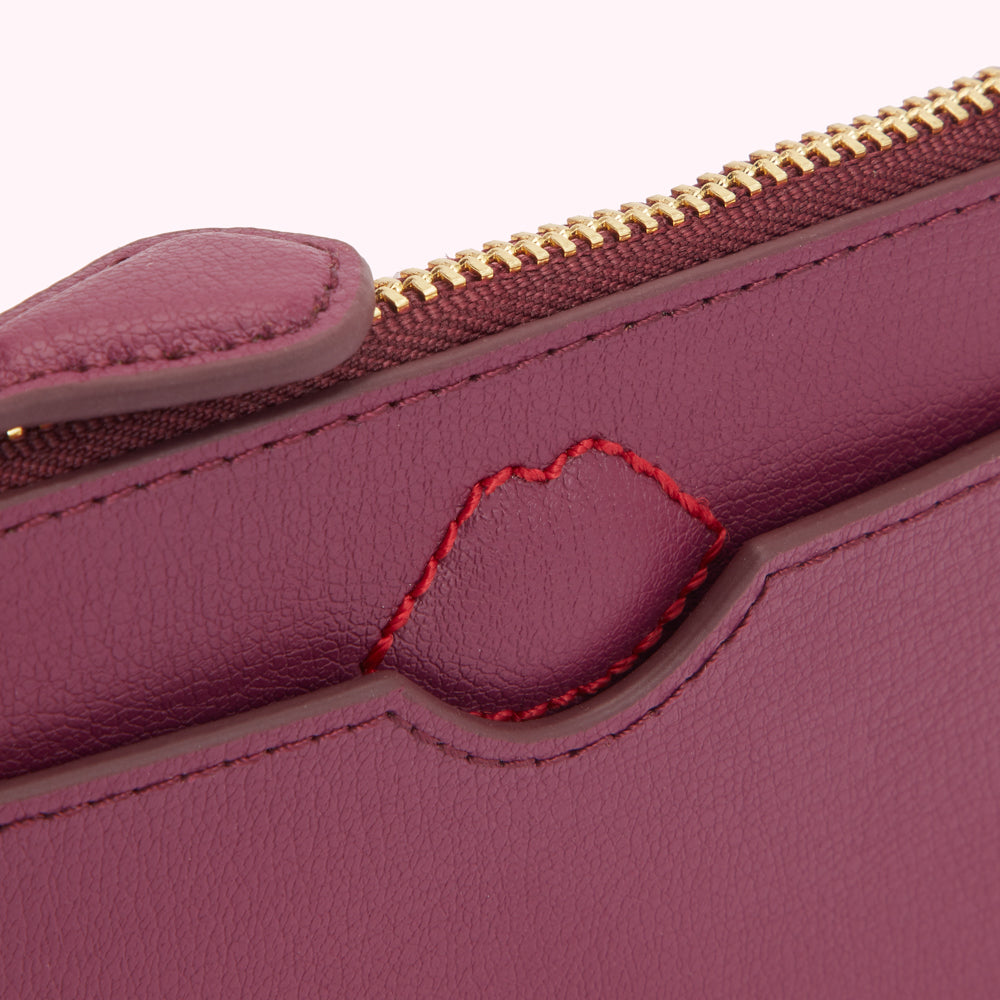 Close-up of a burgundy leather purse with a gold zipper and a red stitched heart detail.
