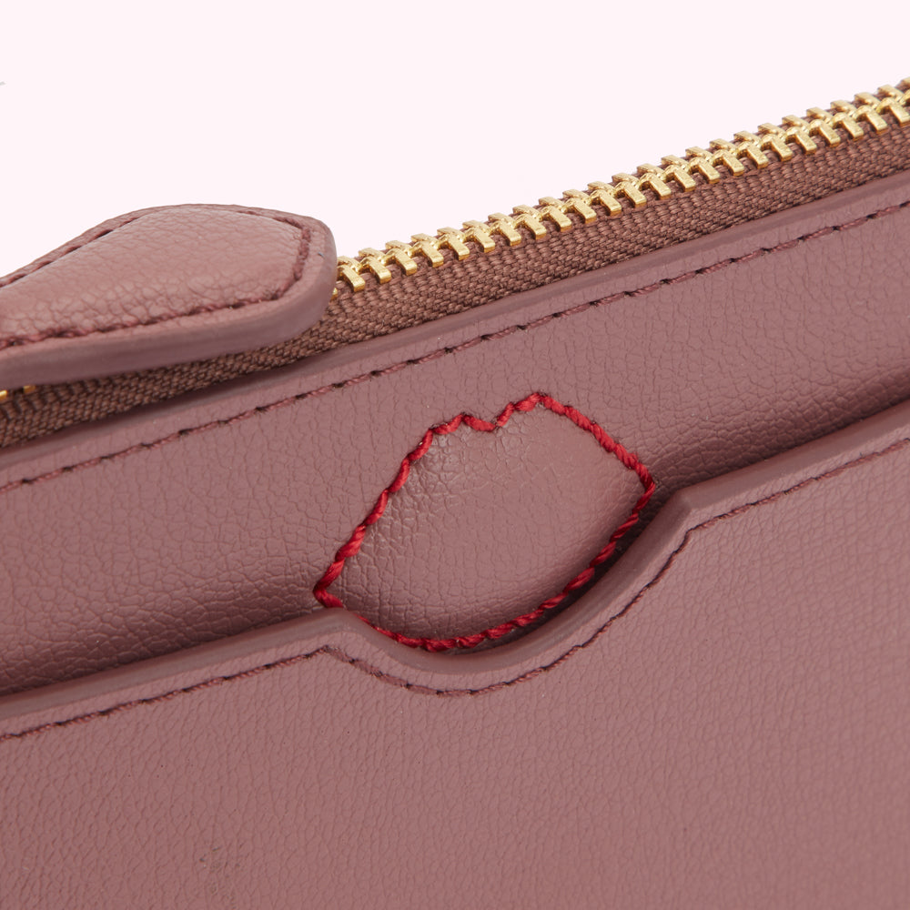 Close-up of a mauve leather purse with a red stitched lip detail and gold zipper.
