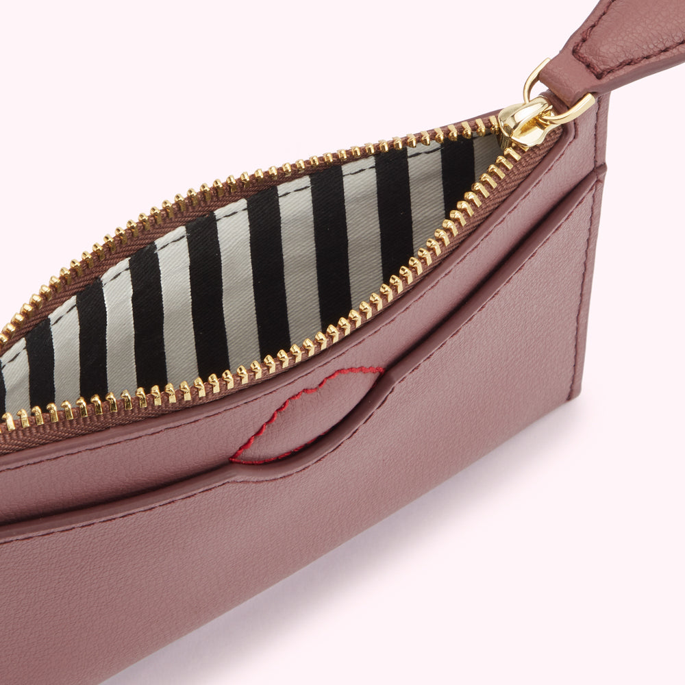 Dusty rose pink leather zip pouch with black and white striped lining and red lip detail.
