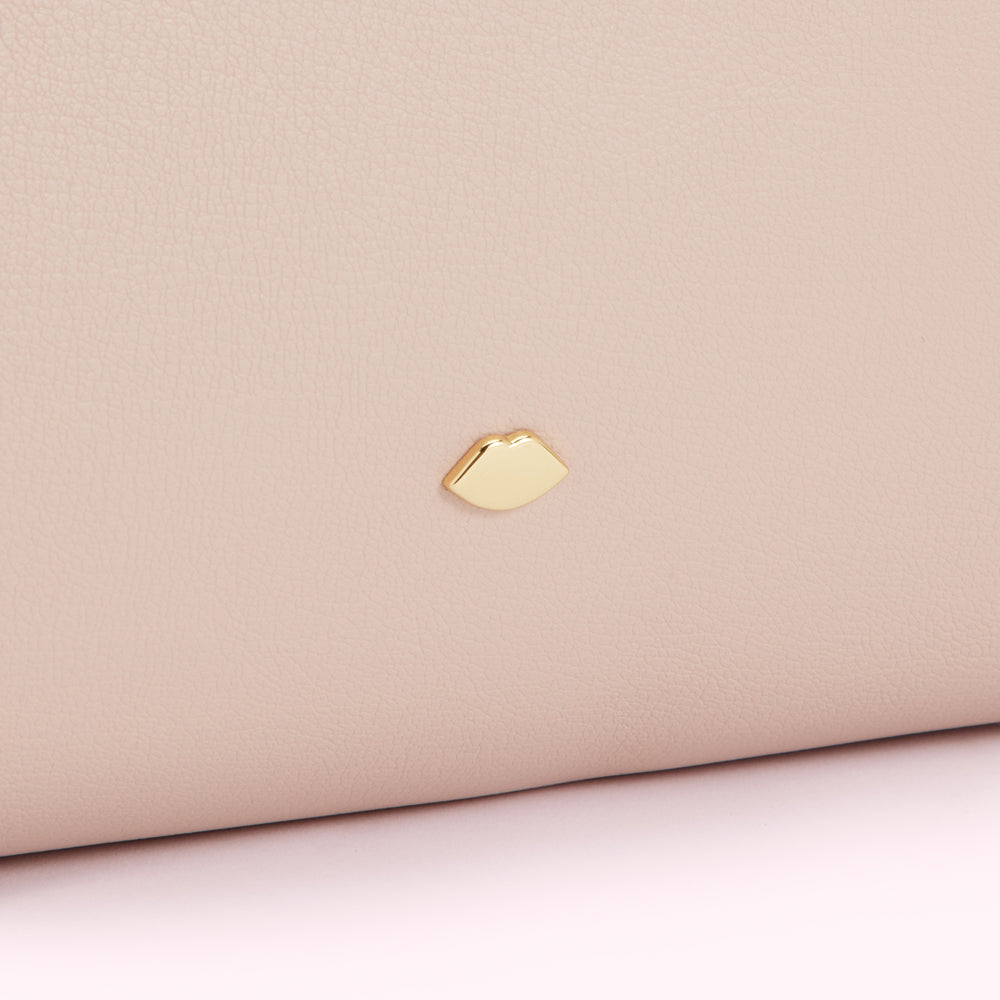 Close-up of a blush pink leather purse with a gold lip-shaped logo.
