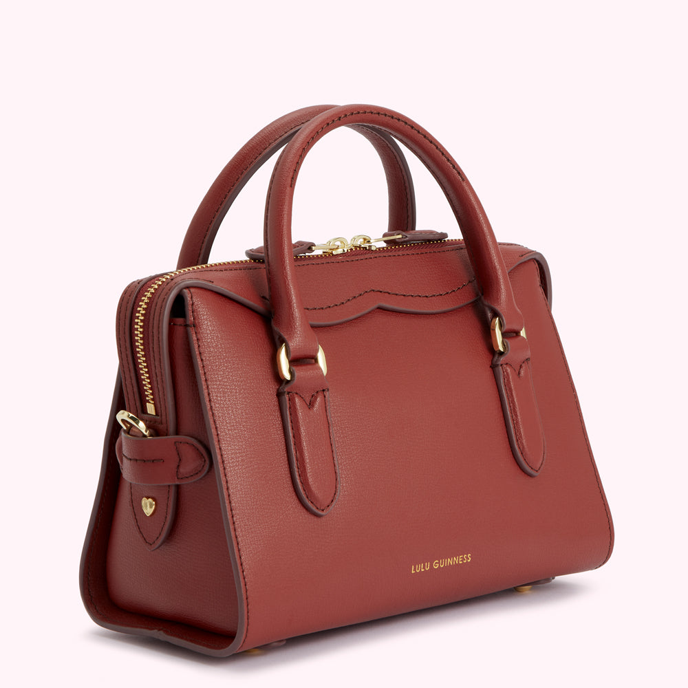A maroon Lulu Guinness leather handbag with gold hardware and a top zip closure.
