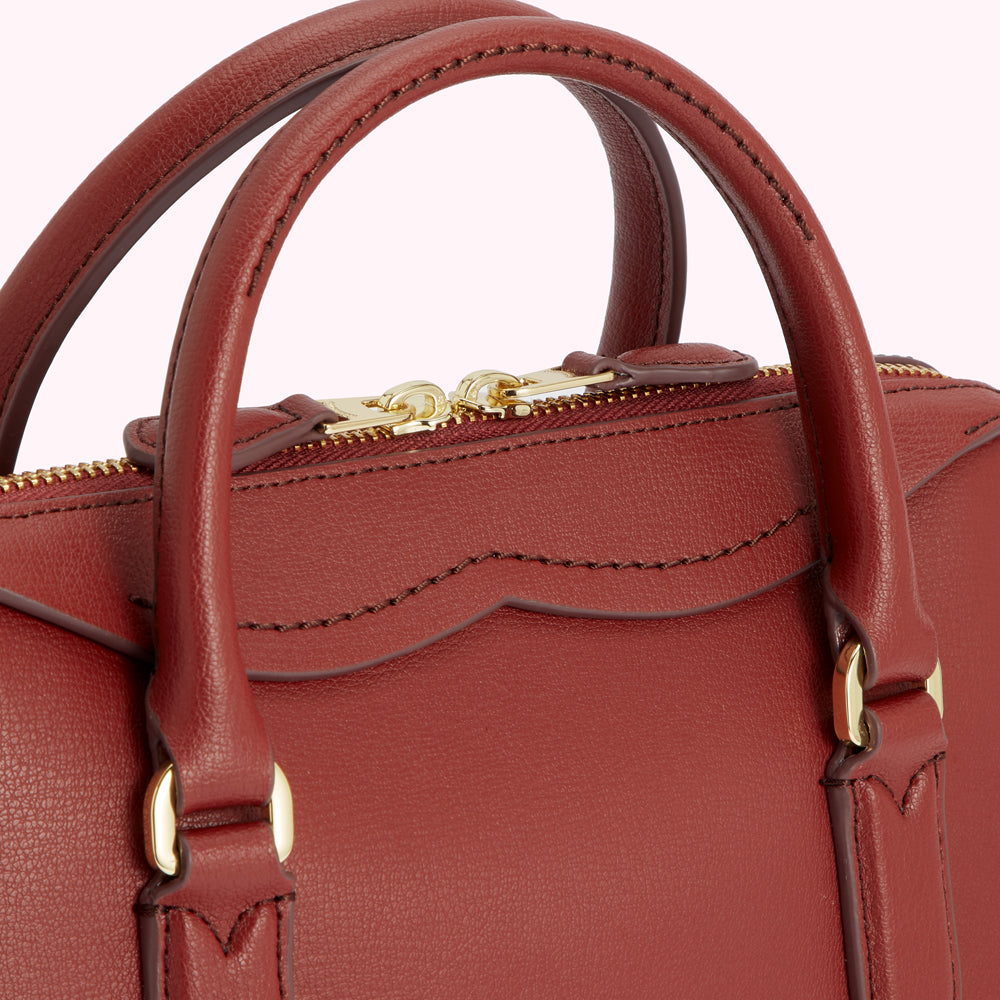 Close-up of a burgundy leather handbag with gold zipper and handles.
