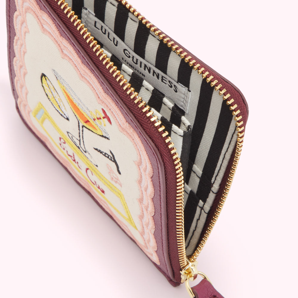 Burgundy zip-around purse with embroidered cocktail design and Lulu Guinness London label visible inside.
