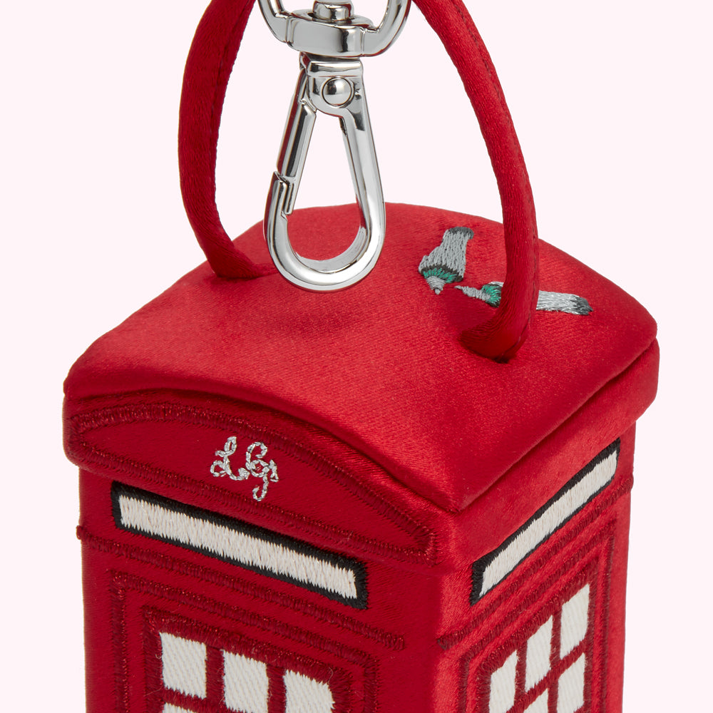 Close-up of a red velvet London telephone booth-shaped keychain with embroidered details and a silver clasp.