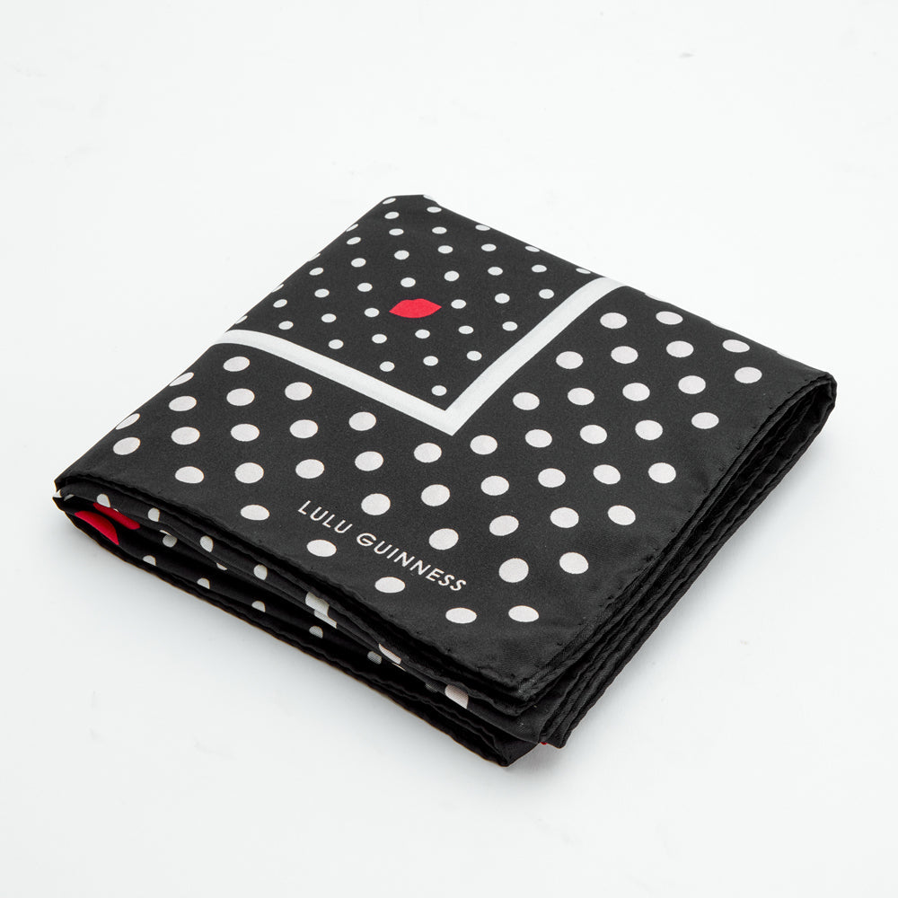 Black silk scarf with white polka dots and a red lip print; folded. The Lulu Guinness logo is visible.
