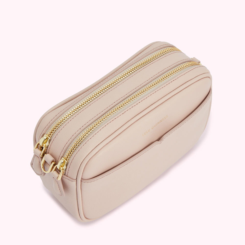 A blush pink Lulu Guinness crossbody bag with two gold zippers.